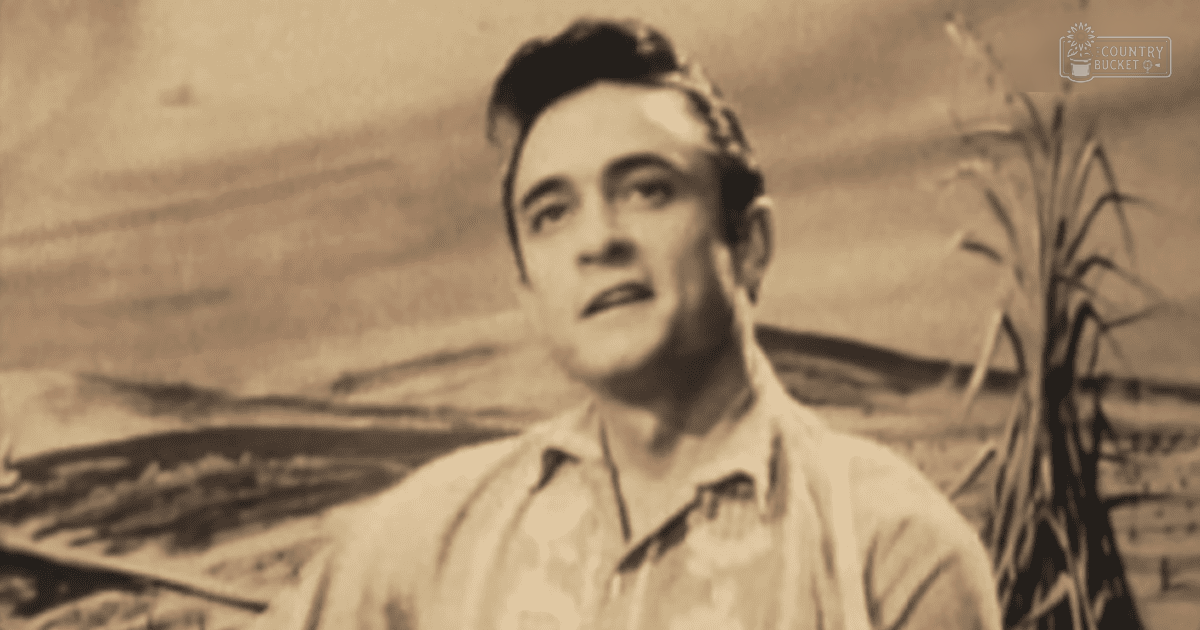 Young adult male wearing light-colored tropical-patterned shirt outdoors near water and vegetation under overcast sky with 'Madly Odd' watermark in corner.