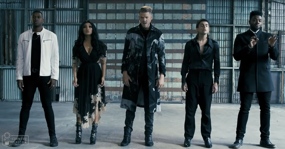 Group of performers in an industrial setting with metal walls and flooring; winter attire suggests cold season.