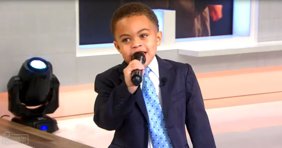 A young child in formal attire stands indoors, possibly on a stage for a performance.
