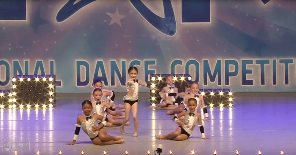 Children performing at an indoor dance competition with a starry backdrop and reflective stage floor.