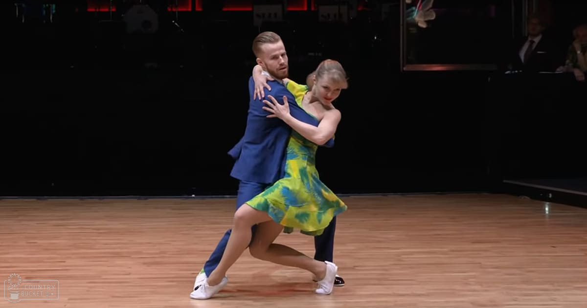 A dance couple performing in a ballroom setting with spectators watching.