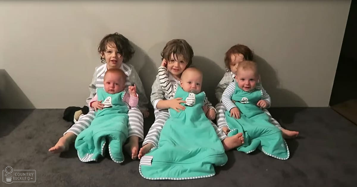 Three toddlers in striped pajamas and teal sleeping bags, standing indoors in a home setting.