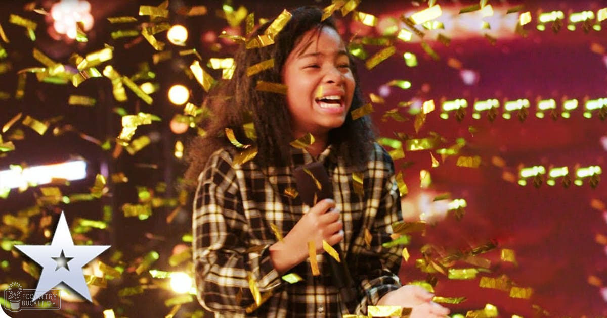 A young adult child with long dark hair wearing a plaid shirt stands against a dark backdrop with confetti falling around them.