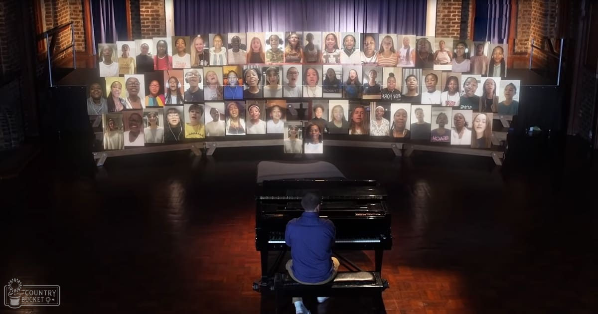 A pianist playing in front of a large screen displaying multiple participants in an indoor performance space with dimly lit curtains and brick walls.