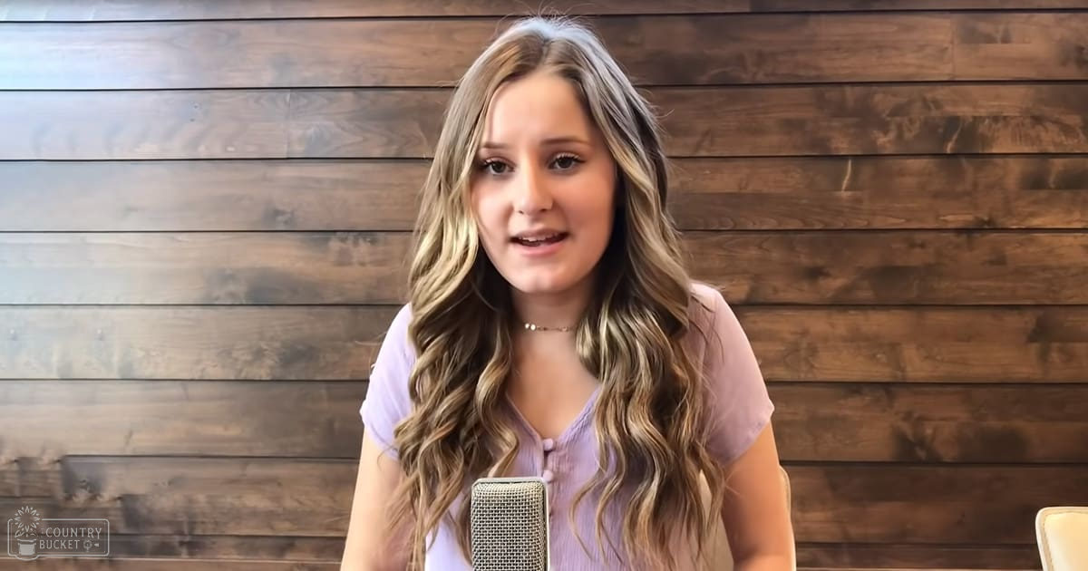 Young adult female in a relaxed indoor setting with a wooden backdrop and partial view of a white chair.