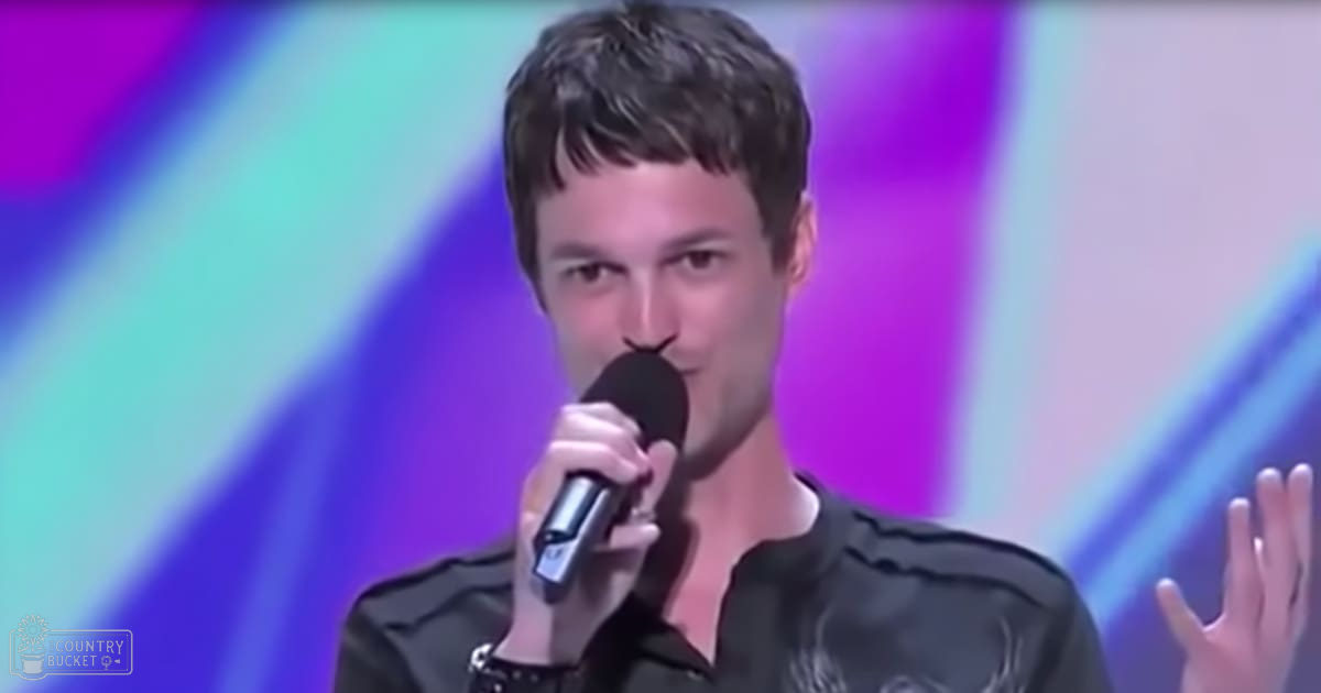 A young adult male is performing in a modern casual setting with vibrant abstract lighting effects, wearing a relaxed fit collared dark gray/black shirt.