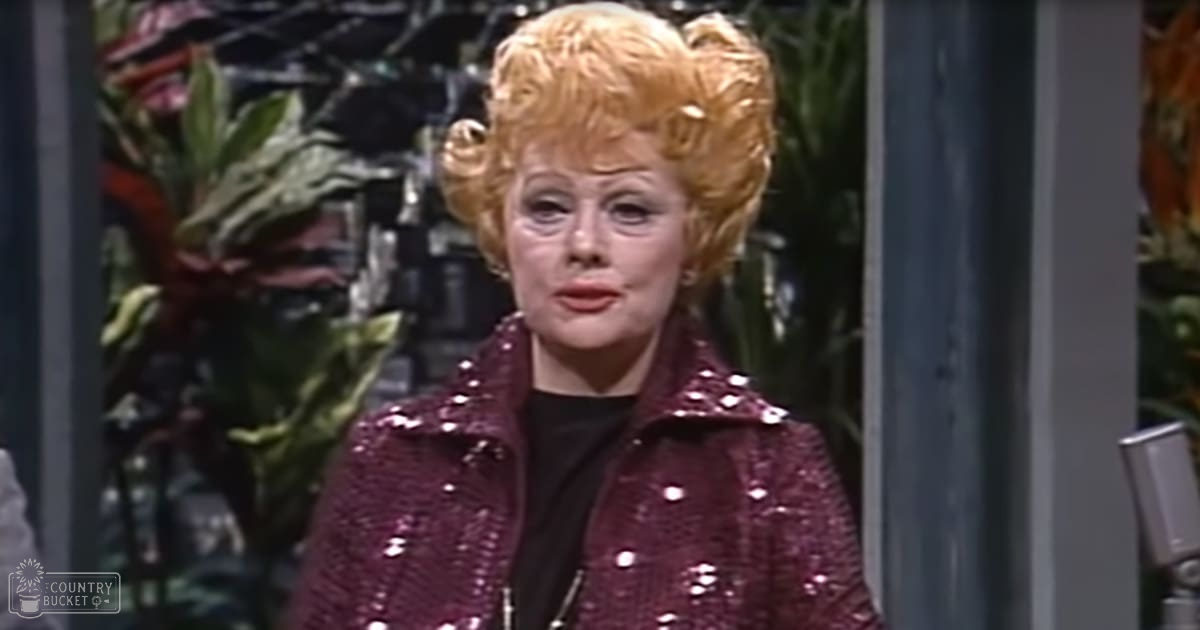 Middle-aged woman wearing a maroon sequined jacket indoors with plants and stage equipment in the background, well-lit artificial lighting.