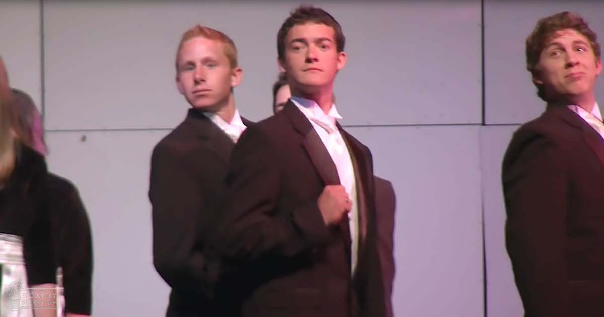 Young adults in formal attire at an indoor event, with artificial lighting and a plain background.