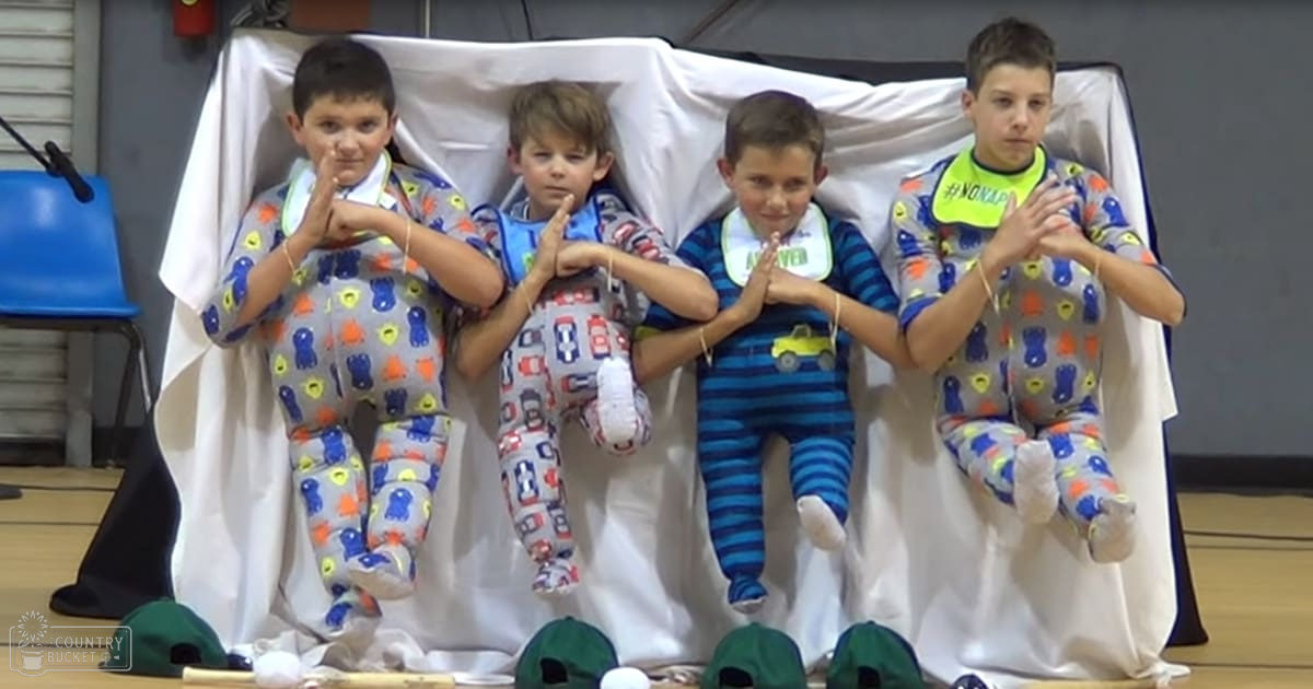 A group of children wearing matching pajamas with colorful patterns, seated indoors in what appears to be an event or school setting.