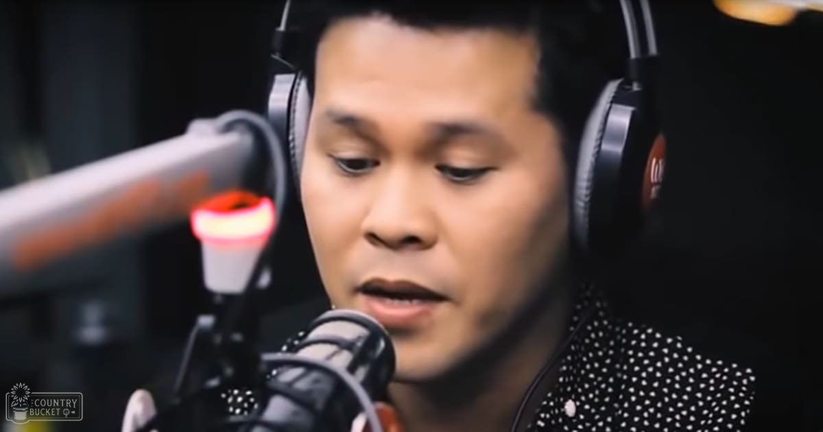 Young adult male wearing a black, long-sleeved, collarless jacket with white polka dots in what appears to be a recording studio environment.