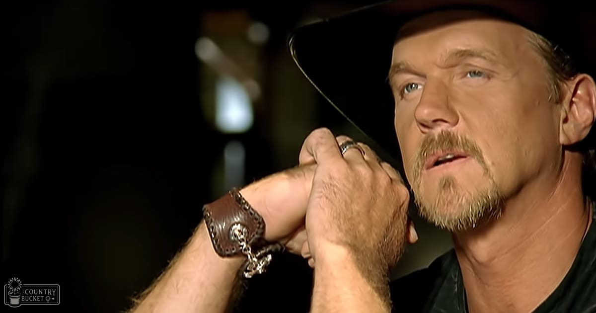 A middle-aged man wearing a dark-colored shirt indoors, holding hands with two rings visible on his fingers.
