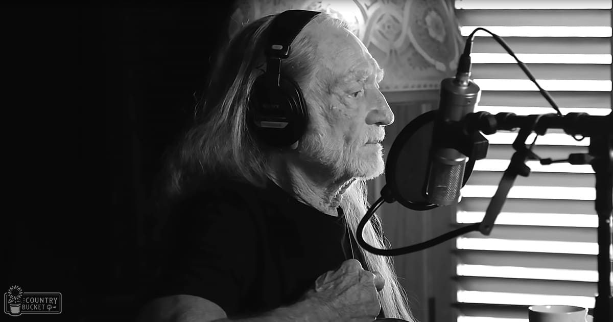 Older adult male in a recording studio with headphones, holding a pen, surrounded by equipment like a microphone and a coffee cup.