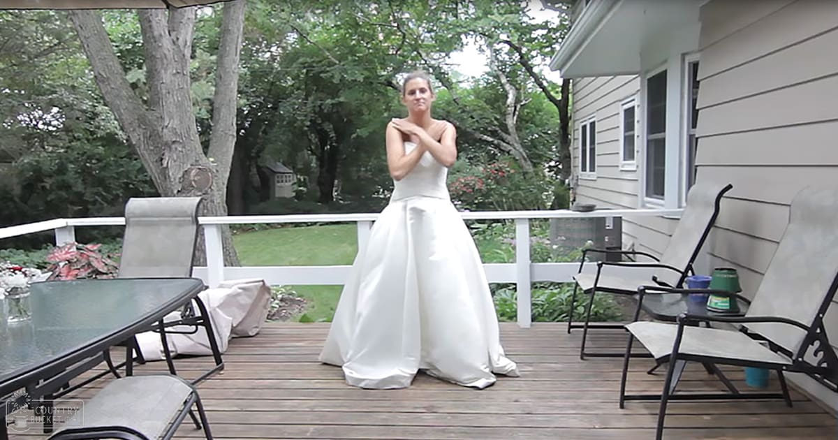 A young adult female in a modern white wedding dress stands on a wooden deck outside her house during spring or summer with soft evening light.