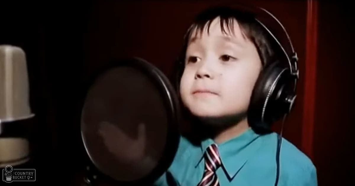 A young child wearing headphones and a teal striped tie in an indoor recording studio setting with focused lighting.
