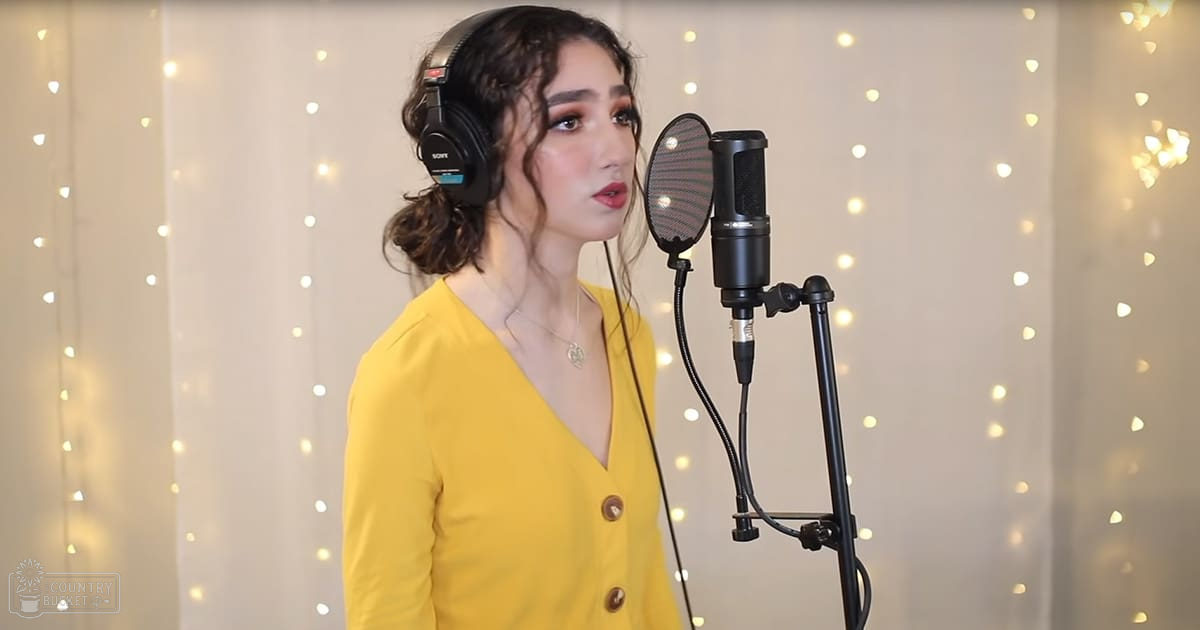 A young adult female wearing a bright yellow button-up top with a deep V-neck and short sleeves, accessorized with large black Sony headphones and a necklace in a recording studio setting.