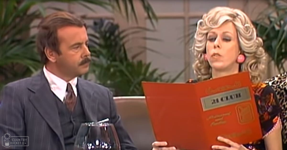 A comedic scene set in an indoor studio environment with green plants and even, bright lighting typical of television production settings.