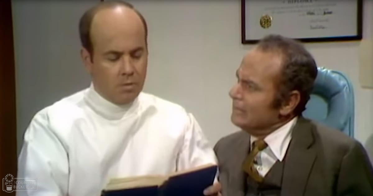A man in a white robe stands beside another man in a dark suit, both in an office setting with a blue chair and framed certificate on display.