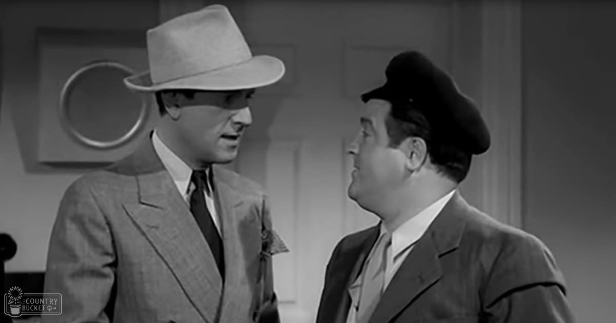 Two adults in suits with hats indoors; one wearing a light-colored suit jacket and dark tie with a white hat, the other in a darker suit with a light tie and beret-style hat.