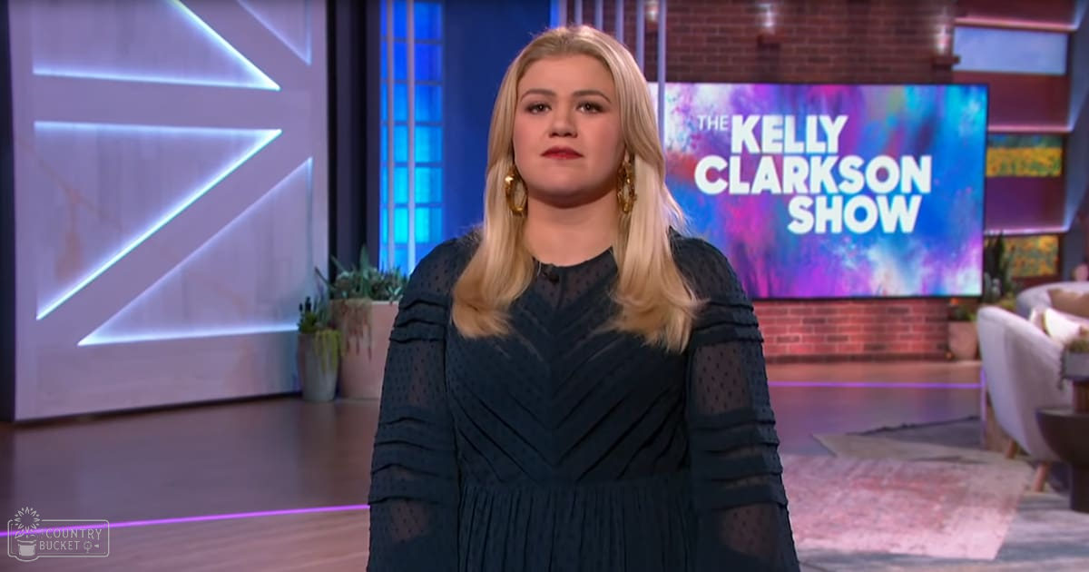 A young adult female wearing a dark teal polka-dotted long-sleeved dress in 'The Kelly Clarkson Show' studio setting with white armchair and colorful backdrop.