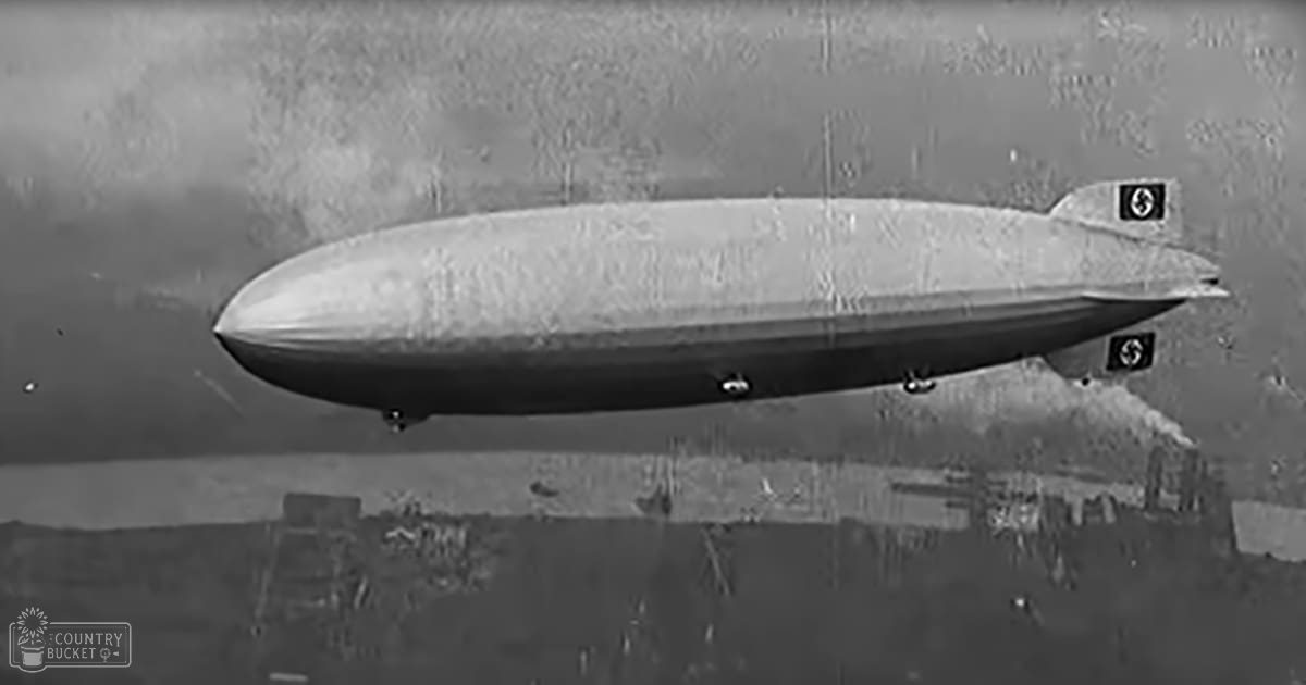 A zeppelin in an urban cityscape with buildings below, possibly early 20th century, natural lighting on overcast day