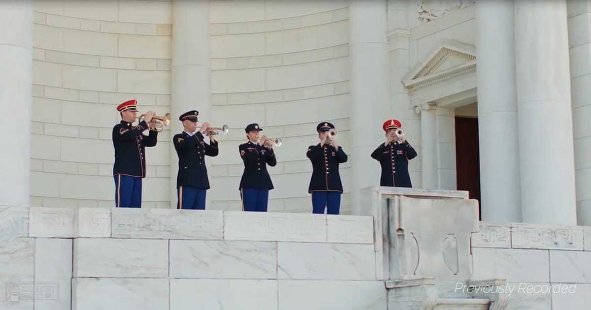 Adult male musicians in dark blue military uniforms with gold trim, playing trumpets at a memorial site with white marble columns and steps.