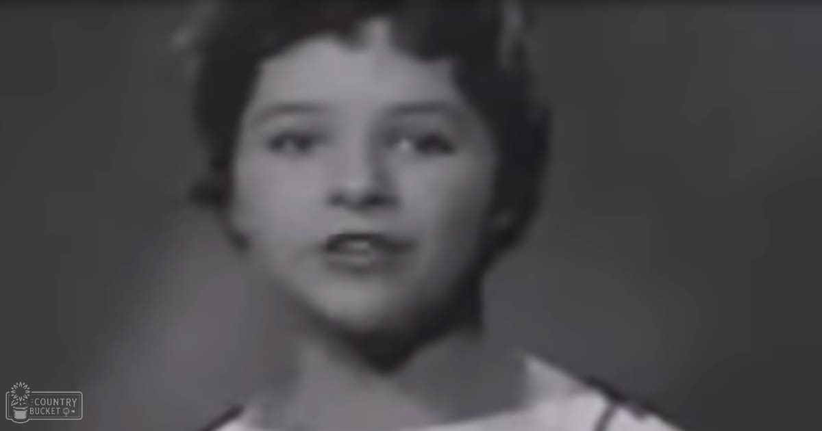 A young female child wearing a patterned white dress indoors with natural lighting.