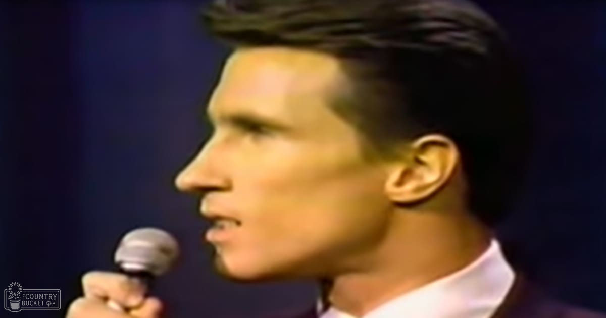 A young adult male in a formal shirt and jacket performs on stage at night.