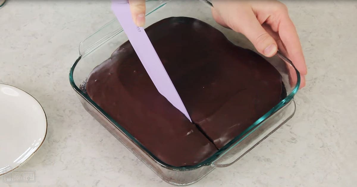 Adult female cutting chocolate in a glass baking dish on a clear countertop in a kitchen setting.