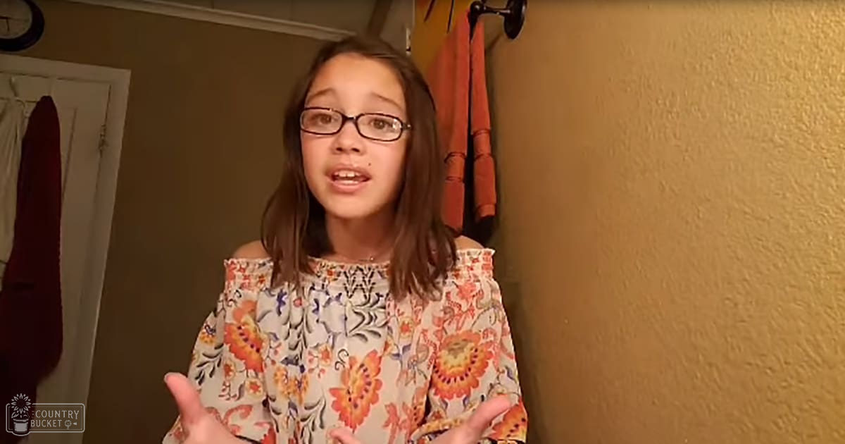 A child wearing a flowy off-the-shoulder blouse with ruffled details at the shoulders, standing indoors in what appears to be a home setting.