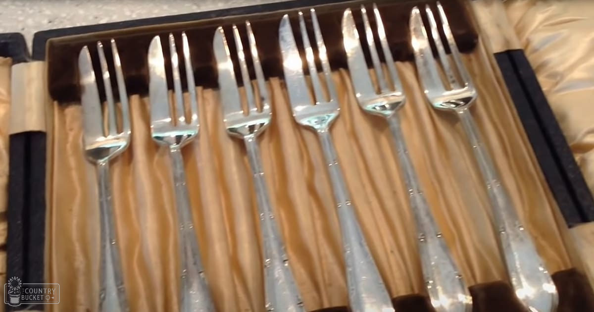 A set of silver forks and knives neatly arranged inside a wooden box lined with beige fabric, possibly silk or satin.
