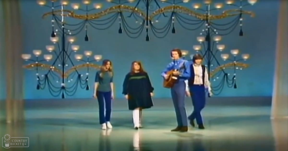 A group of performers on stage with chandeliers and a blue backdrop in an indoor venue.
