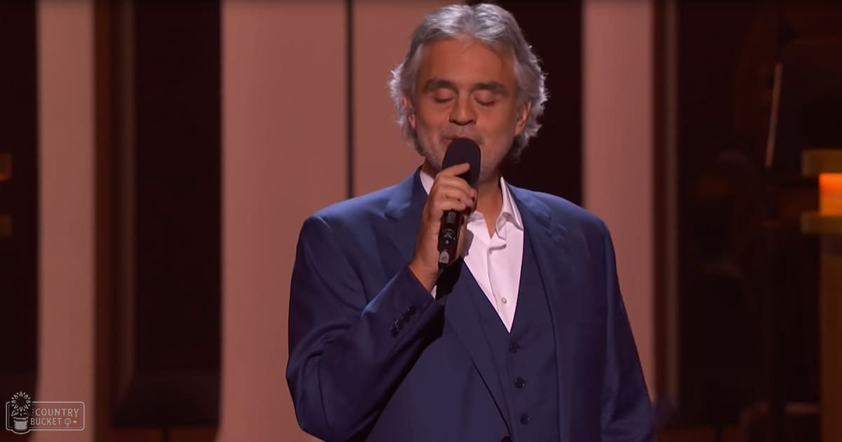 A middle-aged man singing into a microphone, dressed in a dark blue suit and white button-up shirt on stage.