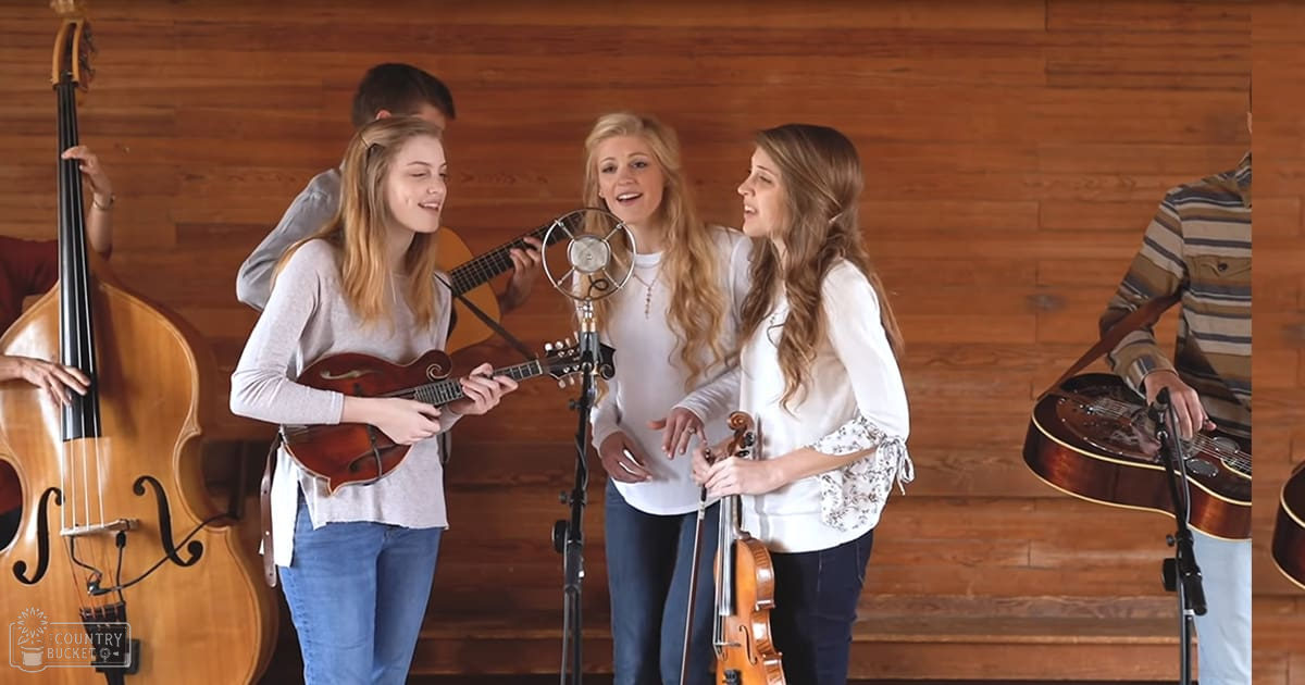 A group of young adults performing music indoors with instruments like a mandolin, violin, double bass, and acoustic guitar.