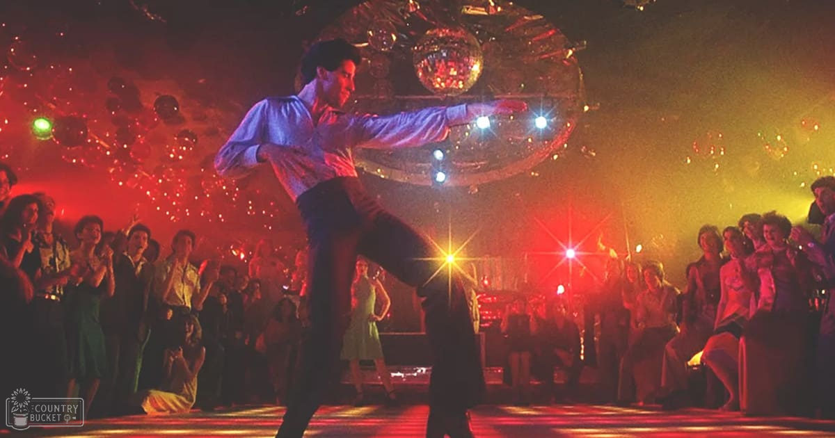 A man in a lively nightclub setting performs a dance move as an adult female in a light-colored dress claps or cheers nearby.