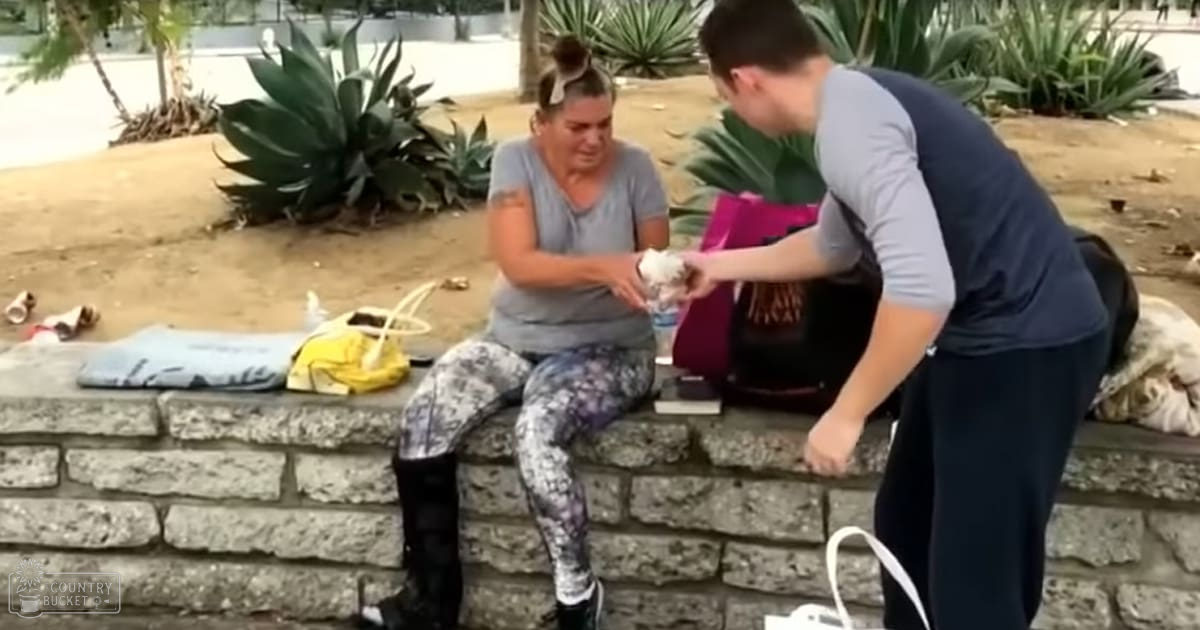 Middle-aged female sits on a stone wall in an outdoor park setting, holding small object; young adult female bends nearby, wearing loose-fitting t-shirt and leggings with text 'FASHION' visible.