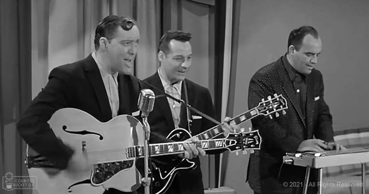 Adult males in mid-20th century suits performing on stage with microphones, suggesting a musical or theatrical performance from the 1950s or early 1960s.