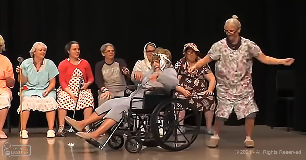 A performance scene with multiple older adult females and males on an indoor stage at night.