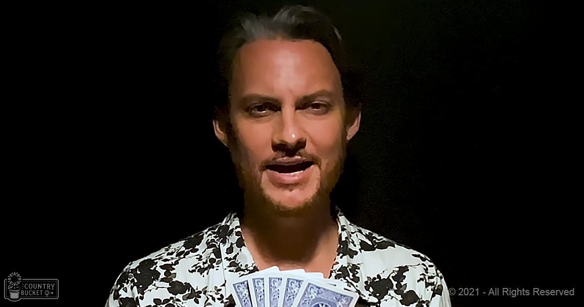 A young adult male in a relaxed fit, collared, short-sleeved, white floral print shirt indoors with dark lighting.