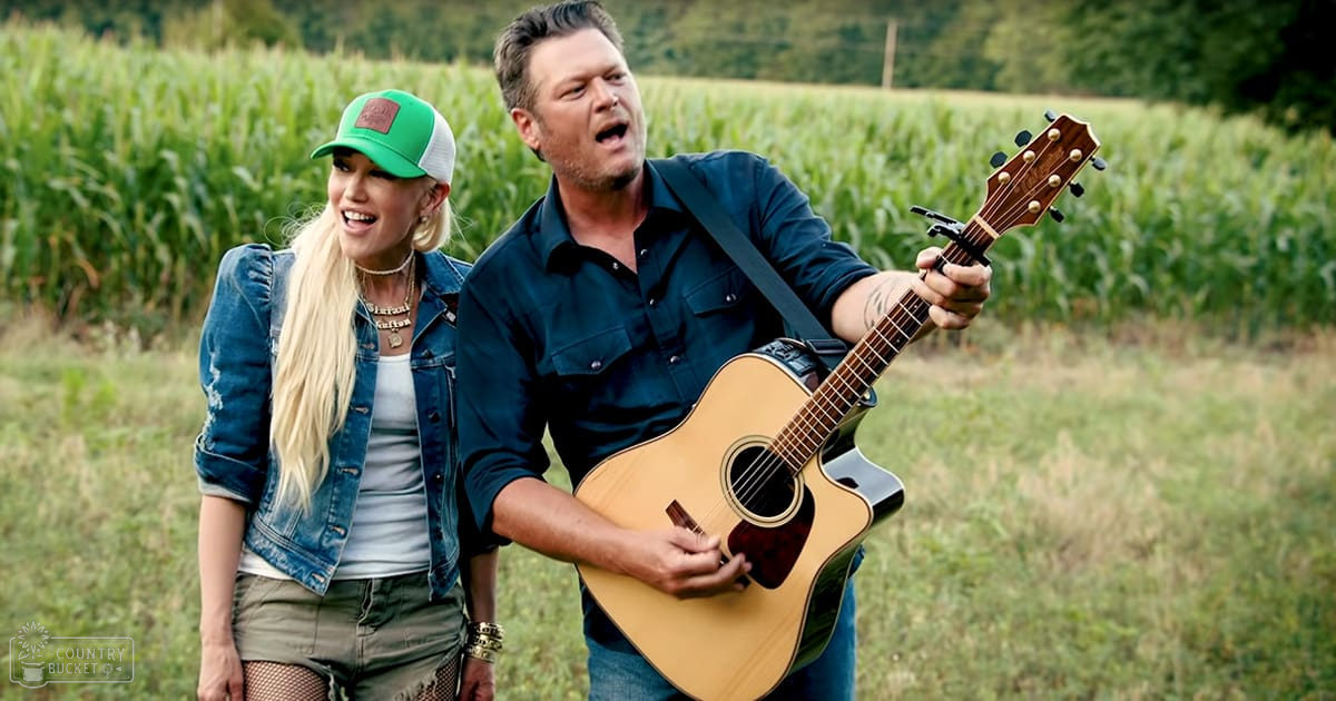 A musical duo in an outdoor rural setting with cornfields, late summer or early fall attire, soft morning or evening light. Both individuals wear bracelets and layered necklaces; one holds a light brown acoustic guitar.