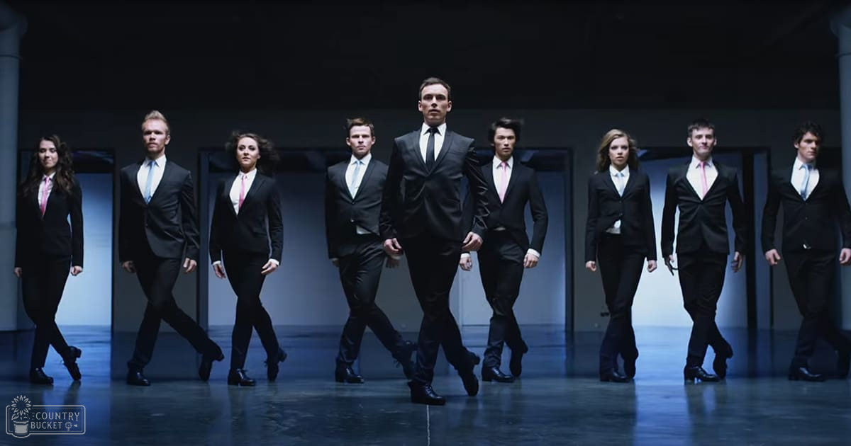 Group of individuals dressed in formal attire, standing indoors with a neutral background and even lighting.