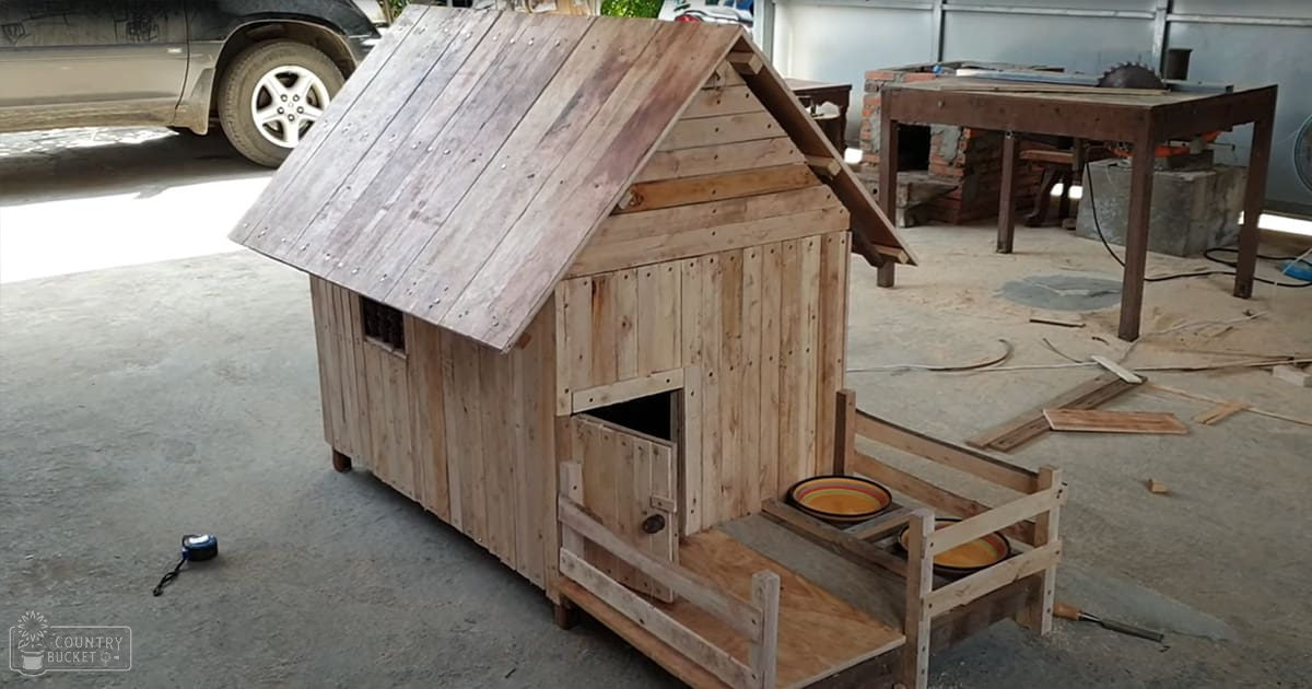 An outdoor workshop with a wooden doghouse, ceramic bowls, tools, and concrete flooring under natural daylight