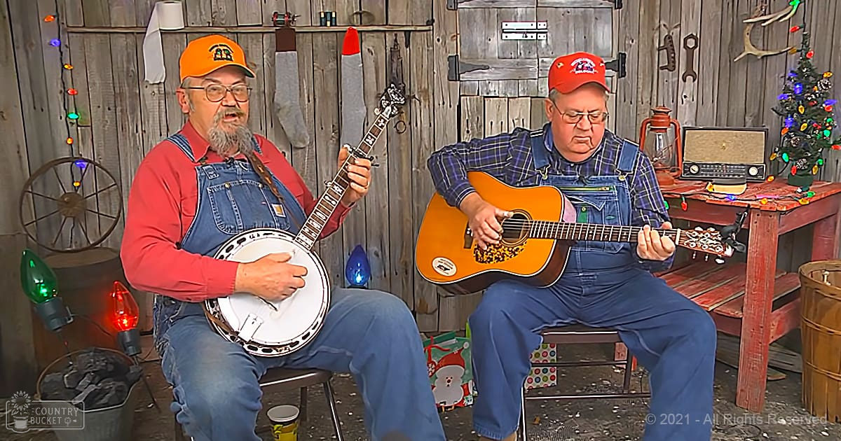 Two older adults playing musical instruments indoors, rustic cabin setting with Christmas decorations.