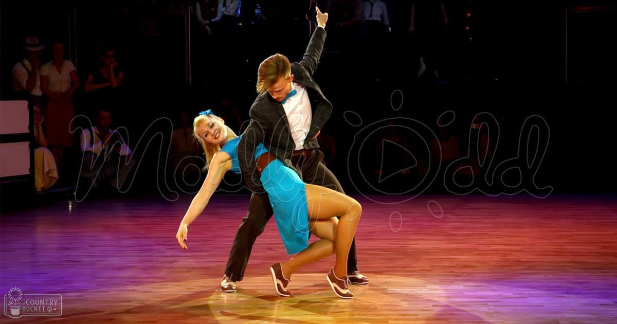 A dance couple performing on a ballroom stage with an audience in the background, illuminated by stage lights at night.