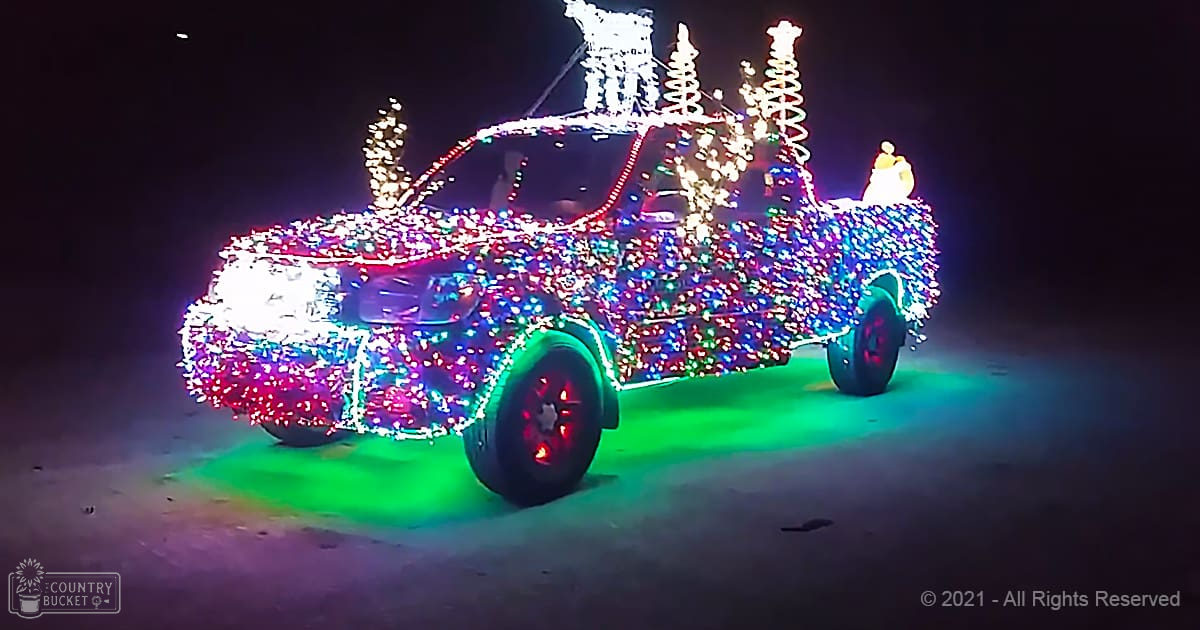 A decorated pickup truck at night with colorful holiday lights adorning it, set against a dark sky, likely during winter.
