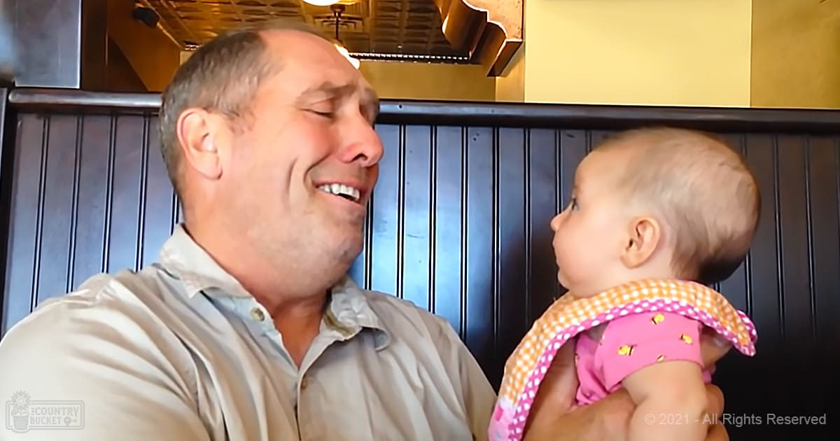 A middle-aged male holding an infant in a restaurant setting with wooden paneling, warm indoor lighting, and pink attire on the child.
