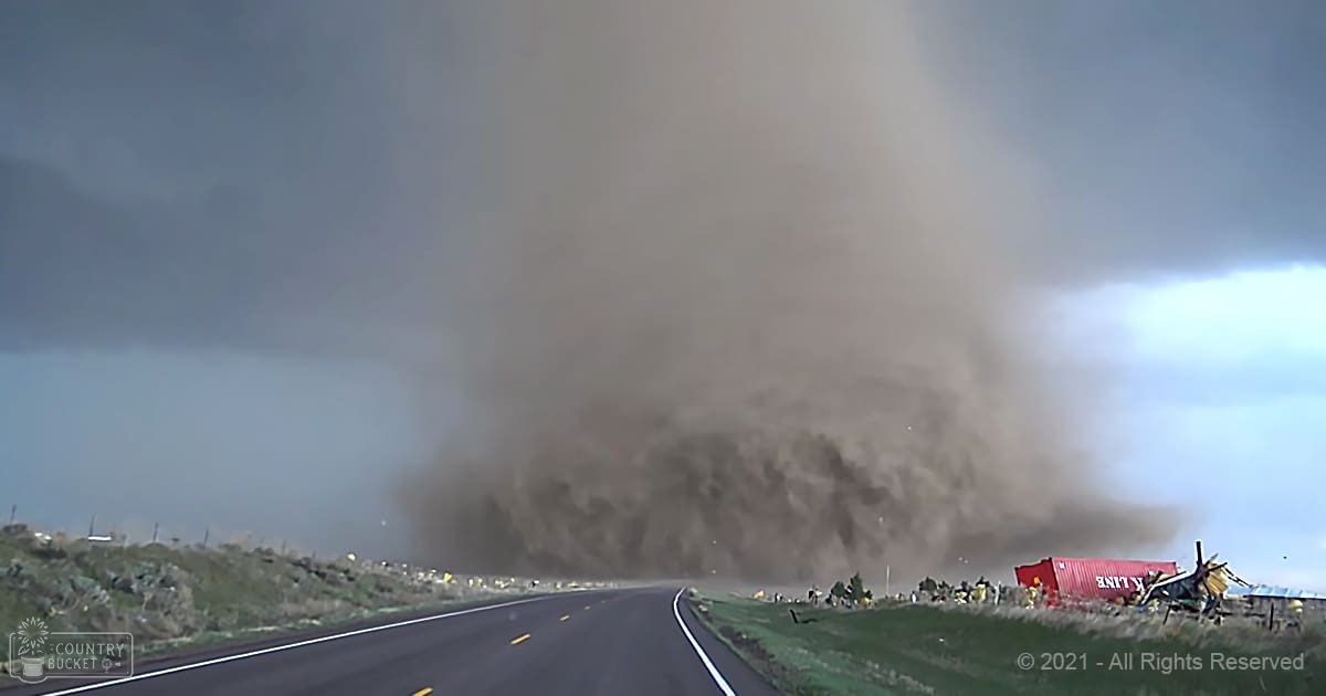 A tornado dominates an open area with a road nearby under overcast daytime conditions.