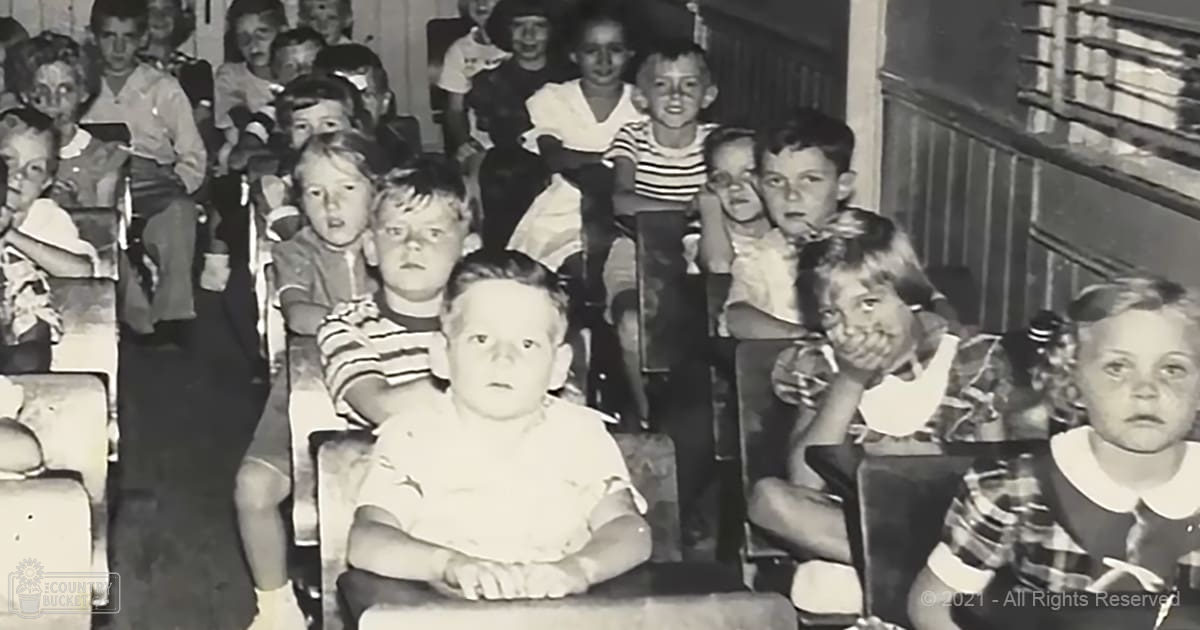 A group of young children indoors, possibly a classroom setting; muted neutral tones with soft lighting suggest an even artificial light source.