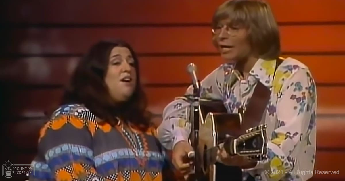 A musical performance scene with two adults on stage under warm lighting; a female in a colorful striped top and male in a floral shirt, surrounded by wooden paneling and red lighting.