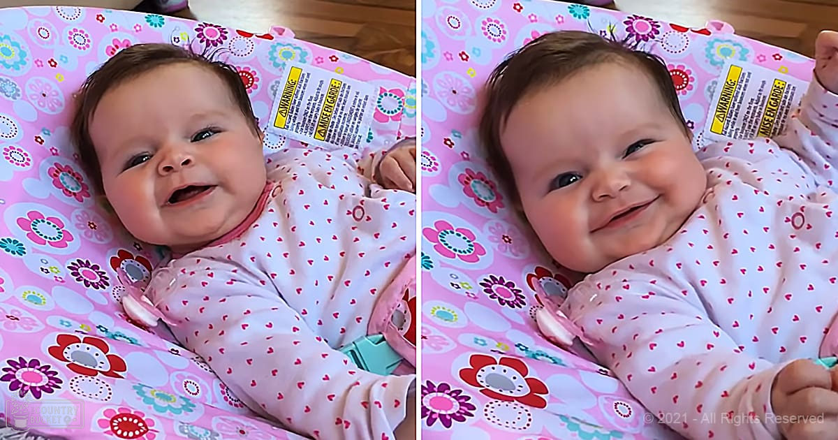 An infant wearing a white long-sleeved onesie with small red heart patterns, indoors in a home environment.