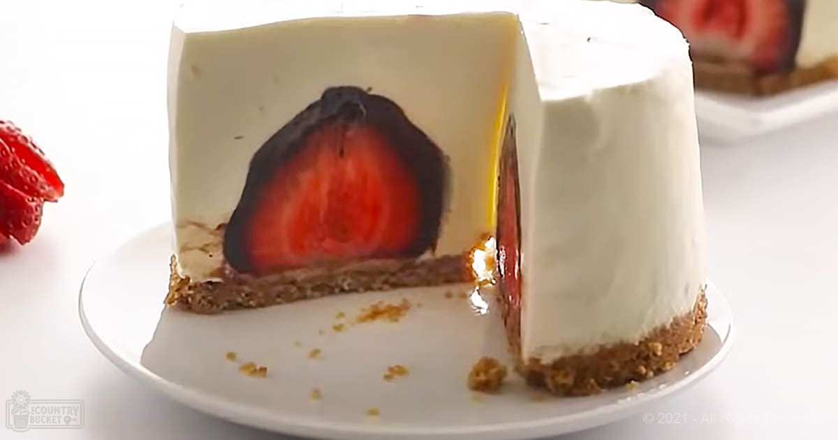 A sliced strawberry cheesecake with a graham cracker crust on a white plate, set indoors under bright even lighting.